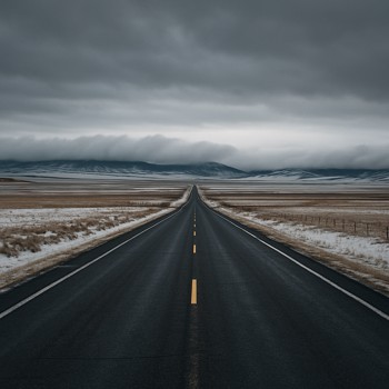 Open winter road leading toward low clouds above distant hills
